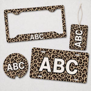 May include: A set of car accessories with a leopard print design. The set includes a license plate frame, license plate, car coaster, and a car air freshener. Each item has the letters "ABC" in white.