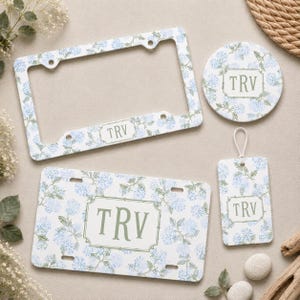 May include: A matching set of accessories featuring a floral hydrangea design in light blue and green on a white background. The set includes a license plate, license plate frame, coaster, and luggage tag, each with the initials "TRV".