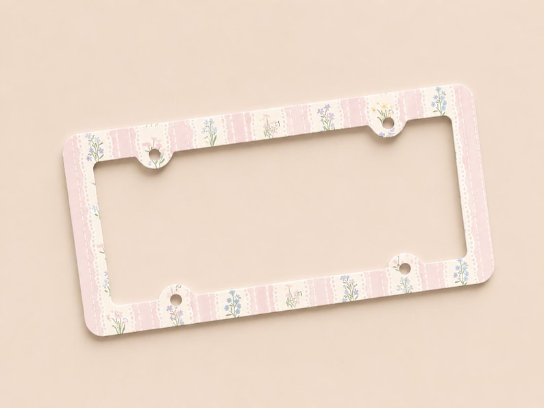 Op de afbeelding: Een rechthoekig kentekenplaatraam met een bloemenontwerp. Het frame heeft een roze en cr&egrave;mekleurig kleurenschema met een herhalend patroon van verticale strepen en kleine bloemen. Het frame heeft vier montagegaten.