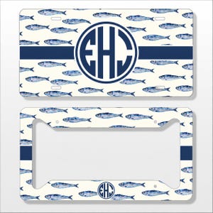 May include: A rectangular license plate and a matching license plate frame, both featuring a cream background with a repeating pattern of blue watercolor sardines. A horizontal navy blue stripe crosses the center, with a circular navy monogram EHC.