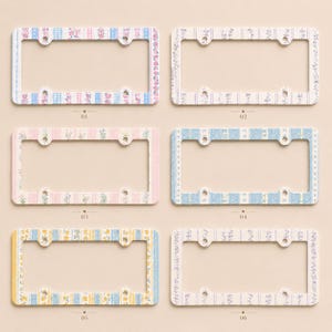 Op de afbeelding: Zes decoratieve kentekenplaathouders met bloemen- en patroonontwerpen. De frames hebben pastelkleuren zoals blauw, roze en geel, met verschillende bloemen- en geometrische patronen. Elk frame heeft montagegaten.