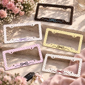 May include: Five rectangular license plate frames featuring polka dot patterns and a central bow graphic. The frames are available in black with blue dots, white with purple dots, yellow with black dots, pink with black dots, and white with red dots.