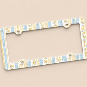 Op de afbeelding: Een decoratief kentekenplaatraam met een bloemen- en streepjespatroon in geel en blauw. Het frame heeft een witte achtergrond en is ontworpen voor een standaard kentekenplaat. Het frame heeft vier montagegaten.