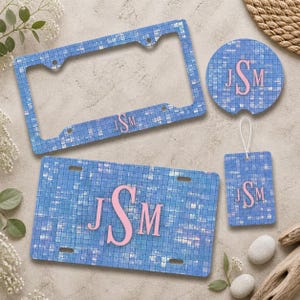 May include: A set of blue mosaic-patterned car accessories, including a license plate, frame, coaster, and tag. Each item features the pink initials "JSM". The accessories are designed with a light blue and white color scheme.