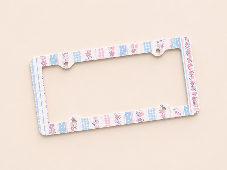 Op de afbeelding: Een rechthoekig kentekenplaatraam met een bloemen- en ruitpatroon in pastelroze en blauw. Het frame heeft een witte achtergrond en vier montagegaten.