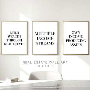 May include: Three framed wall art prints with gold frames and white backgrounds. Each print features black text: "Build Wealth Through Real Estate," "Multiple Income Streams," and "Own Income Producing Assets." The text "Real Estate Wall Art Set of 6" is below.