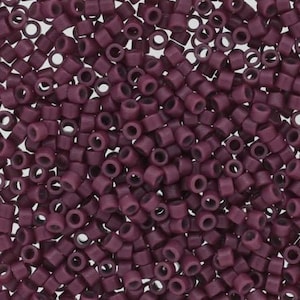 May include: A close-up view of a large quantity of small, round, dark purple beads. The beads have a hole in the center and are made of a smooth, opaque material.