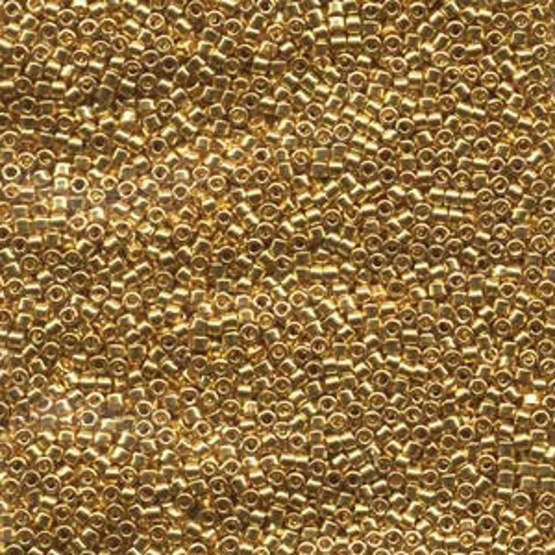 May include: A close-up view of a large quantity of small, gold-colored seed beads. The beads are uniform in size and shape, and they are arranged in a random pattern.