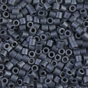 May include: A close-up view of a large quantity of small, dark gray, cylindrical beads. The beads have a hole in the center and are arranged in a random pattern.