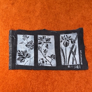 May include: A rectangular black fabric patch featuring three distinct white rectangular panels, each displaying a different botanical illustration of flowers and leaves. The left edge has a white serged stitch finish, and the text Stampin' Up! is printed vertically in the bottom right corner.