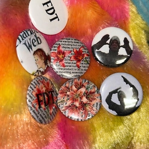 May include: A collection of six circular pin-back buttons featuring various designs. One button is white with black text reading FDT. Others display a person with the text World Wide Web, a person making a hand gesture, floral prints, and FDT text.