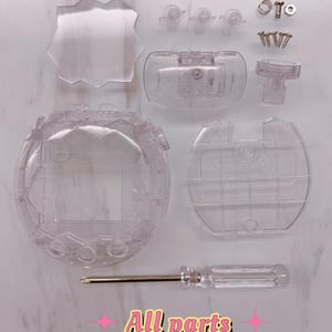 Peut inclure: Un ensemble de composants en plastique transparent pailleté pour un appareil de jeu électronique, comprenant une coque principale, un couvercle, des boutons, des vis, un ressort et un petit tournevis. Le texte "All parts" est écrit en rose.
