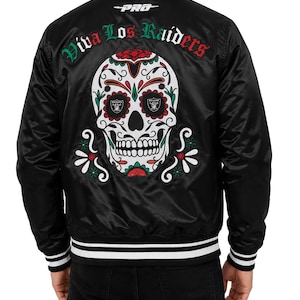 Może przedstawiać: Czarna satynowa kurtka typu varsity z dużym haftowanym motywem czaszki na plecach w kolorach czerwonym, zielonym i białym. Napis "PRO" oraz "Viva Los Raiders" wyhaftowano nad czaszką, która zawiera dwa logotypy drużyny Raiders.
