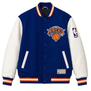 Könnte beinhalten: Eine blaue Collegejacke mit weißen Ärmeln, die das New York Knicks-Logo auf der Brust, einen NBA-Aufnäher am linken Ärmel und ein Hardwood Classics-Etikett am Saum zeigt. Die Jacke hat eine Druckknopfleiste und gestreifte Rippstrickbündchen.