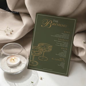 May include: A rectangular bar menu card with a dark olive green background and gold text. The menu features sections for Wine, Spirits, Beer, and Non-Alcoholic drinks, with gold line art of two cocktail glasses and the text "THE BAR MENU".