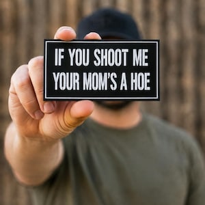 May include: A rectangular black patch with a white border and white text that reads IF YOU SHOOT ME YOUR MOM'S A HOE. The patch features a clean, bold sans-serif font and a high-contrast design, presenting a clear message in a simple, rectangular format.