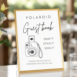 May include: A framed sign with gold trim, featuring the words "POLAROID Guestbook" in elegant script. Below, a line drawing of a Polaroid camera with a graduation cap image. Text reads "SNAP IT, STICK IT, SIGN IT." The bottom says "THANKS FOR HELPING US REMEMBER THIS SPECIAL DAY."