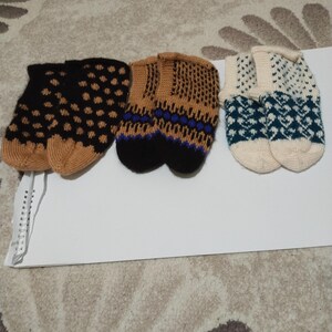 Puede incluir: Tres pares de zapatillas de punto en varios patrones y colores. Un par es negro con lunares color canela, otro es color canela con detalles negros y azules, y el tercero es blanco y verde azulado con un diseño geométrico.
