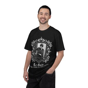 Puede incluir: Camiseta negra con un retrato en blanco y negro dentro de un marco decorativo. El texto "Le Guin" y una cita est&aacute;n impresos debajo. La camiseta la lleva una persona.