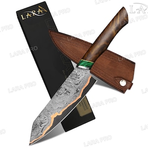 May include: A Damascus steel chef's knife with a wooden handle and a leather sheath. The blade has a unique pattern with a copper-colored edge. The handle is dark wood with a green accent. The knife is presented with its black box.