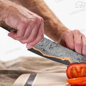 May include: A Damascus steel chef's knife with a wooden handle is slicing a red tomato on a wooden cutting board. The knife blade has a unique pattern with copper accents. The tomato is cut into slices.