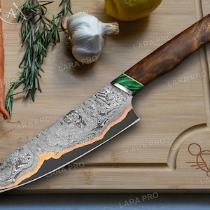 May include: A Damascus steel chef's knife with a dark wood handle and green accents. The blade has a unique pattern and an orange accent line. The knife rests on a bamboo cutting board with carrots, rosemary, and garlic.