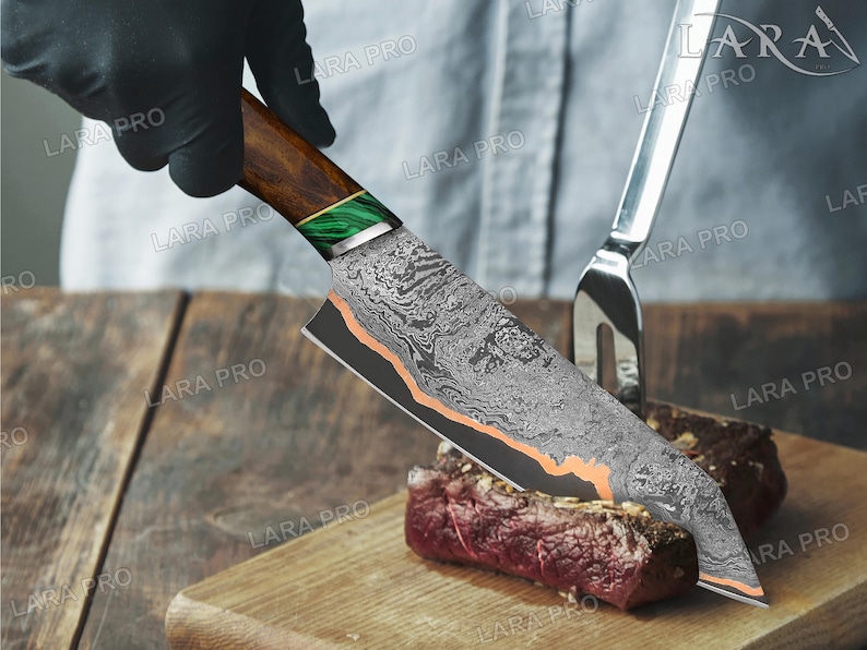 May include: A Damascus steel chef's knife with a wooden handle and green accents is cutting a piece of raw meat on a wooden cutting board. A silver fork is in the background. The knife has a patterned blade and copper-colored accents.