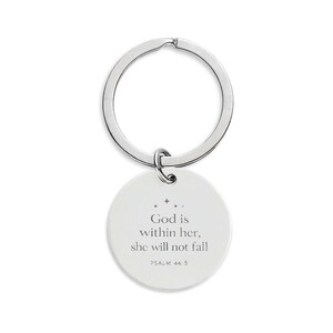 以下が含まれることがあります： 丸い白いペンダントが付いたシルバーカラーのキーホルダー。ペンダントには「God is within her, she will not fall」と「PSALM 46:5」の文字がグレーでプリントされています。シンプルでエレガントなアクセサリーです。