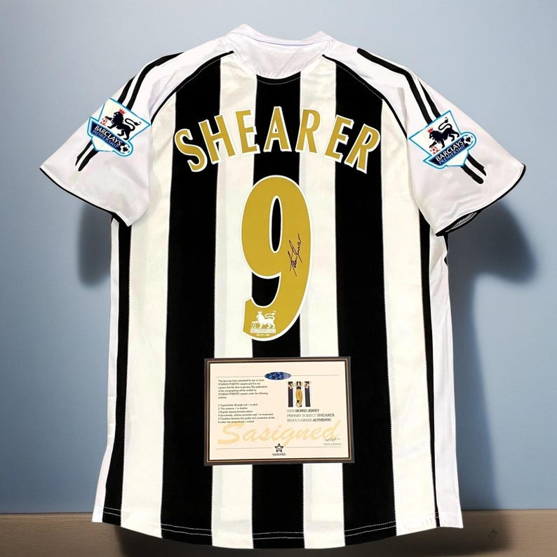 May include: A black and white striped soccer jersey with the name "SHEARER" and the number "9" in gold. The jersey has the Barclays Premier League logo on the sleeves and a certificate of authenticity.