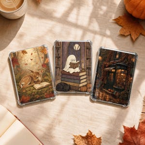 Puede incluir: Tres fundas rectangulares transparentes para teléfono con ilustraciones de temática otoñal. La funda izquierda muestra un cervatillo leyendo en un bosque. La central muestra un fantasma leyendo sobre libros. La derecha muestra el exterior de una tienda.