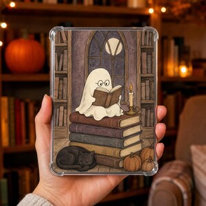 Può includere: Una custodia protettiva trasparente per tablet con l'illustrazione di un fantasma bianco con occhiali tondi che legge un libro seduto sopra una pila di quattro grandi libri. Un gatto nero dorme accanto ai libri vicino a tre piccole zucche arancioni.