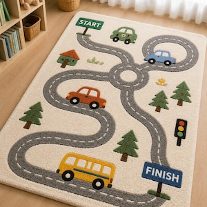 May include: A cream-coloured children's rug with a road design featuring a green "START" sign and a blue "FINISH" sign. The rug has a winding grey road with colourful cars, trees, and a yellow school bus.