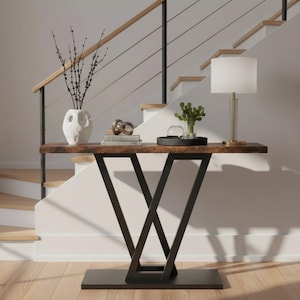 May include: A modern console table with a dark wood top and black metal base. The table is decorated with a white vase, books, a decorative sculpture, a black tray, and a lamp. The table is 60 inches long.