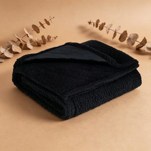 May include: A folded black plush blanket with a soft, textured surface. The blanket is made of a thick, cozy material, perfect for snuggling. The blanket is folded neatly, with a contrasting black fabric visible on the inside.