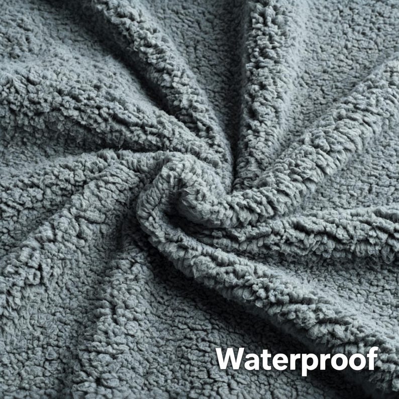 May include: Close-up of a gray, textured fabric with a plush, sherpa-like appearance. The word "Waterproof" is printed in white on the lower right corner. The fabric is folded, showing the depth and texture of the material.