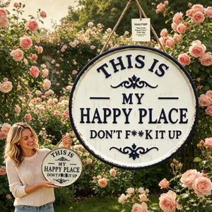 May include: A round, distressed white sign with a navy blue border and the text "THIS IS MY HAPPY PLACE DON'T F**K IT UP." The sign is hanging by a rope and surrounded by pink roses.
