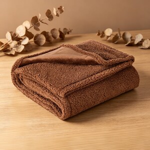 May include: A folded brown blanket with a plush, textured surface. The blanket has a smooth, solid-colored underside and a contrasting, textured top. The blanket is folded neatly, showcasing its soft texture and warm color.