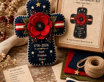 Op de afbeelding: Een DIY viltornament-set met een donkerblauw kruisvormig ornament voorzien van een grote rode klaproos, wit-rode strepen en de tekst 1776-2026 Faith Freedom Honor. De set bevat voorgesneden viltstukken, borduurgaren, vulling, een naald, jute koord, een sterbedel en instructies.