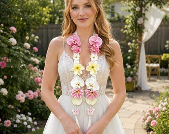 Op de afbeelding: Een witte afstudeerstola met twee verticale stroken versierd met kunstmatige roze, witte en gele bloemen, ronde houten accenten en kleine roze vlinderbedels aan de onderkant, gedragen over een witte mouwloze jurk.