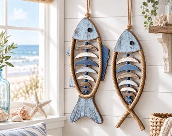 Op de afbeelding: Twee wanddecoraties in de vorm van vissen, gemaakt van verweerd lichtblauw hout en natuurlijk touw. Elke vis heeft een skeletontwerp van gebogen houten segmenten in blauwe en witte tinten, geaccentueerd met kleine donkerblauwe kralen.