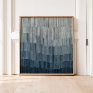 Puede incluir: Obra de arte abstracta enmarcada en madera. La imagen presenta un diseño texturizado con líneas verticales en tonos azules, creando un efecto degradado. Los colores transicionan de azul claro en la parte superior a un azul marino oscuro en la parte inferior. El marco es de color marrón claro.