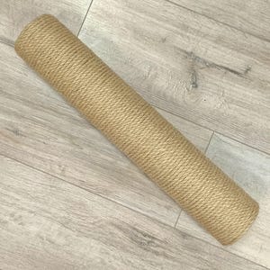 May include: A cylindrical scratching post wrapped in thick, light brown natural jute rope. The object is a long, solid tube with a consistent, tightly coiled texture covering the entire exterior surface from end to end.
