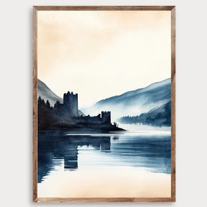 May include: A framed watercolor painting depicting a dark blue silhouette of a castle on a lakeshore, surrounded by mountains and pine trees. The scene features a soft, pale peach sky and a calm, reflective body of water in shades of deep blue.