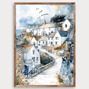 May include: Watercolor painting of a coastal village with white houses, gray rooftops, and stone walls. The artwork features a winding road, a cloudy sky, and a few birds in flight. The painting is framed in a light brown wooden frame.
