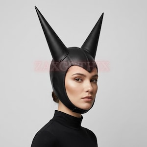 May include: A black leather-like headpiece featuring two tall, pointed horn-like structures extending upward from the crown. The headgear covers the top and sides of the head, securing under the chin with a strap. The text ZAXGOTHIX is visible.