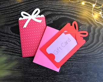 May include: A red gift card holder with a white bow and the words "Gift Card" printed on the front. The holder is made of paper and is folded in half.