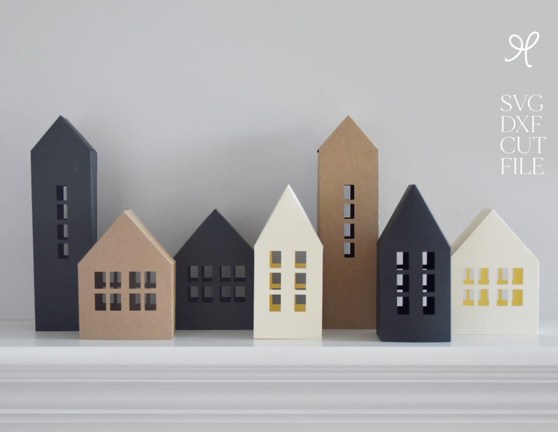 K&ouml;nnte beinhalten: Ein Set aus sieben Papierh&auml;usern in verschiedenen Farben, darunter Schwarz, Braun, Wei&szlig; und Gelb. Die H&auml;user haben Fenster und sind in einer Reihe auf einer wei&szlig;en Oberfl&auml;che angeordnet. SVG DXF CUT FILE.