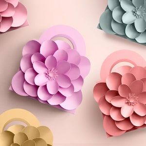 May include: An overhead shot showcases several paper flower-shaped bags in various pastel colors. The bags feature a rounded handle and are arranged on a light pink background. The flowers have multiple layers of petals.