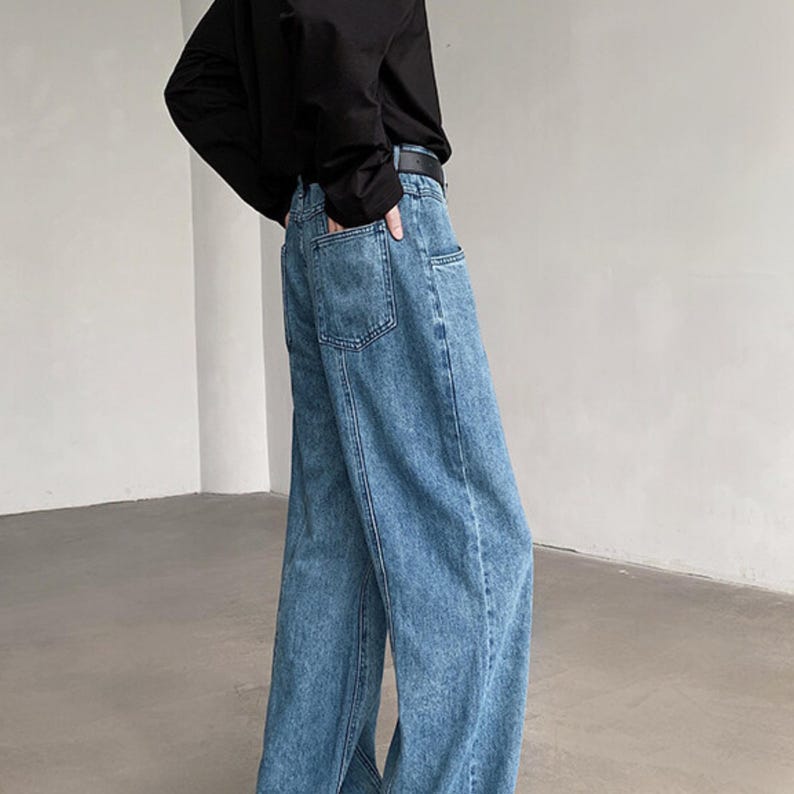 K&ouml;nnte beinhalten: Hellblaue Jeans mit weitem Bein. Die Jeans haben ein klassisches F&uuml;nf-Taschen-Design und einen dunkelblauen G&uuml;rtel. Der Denim hat eine verwaschene Optik, und die Jeans werden mit einem schwarzen Langarmshirt getragen.