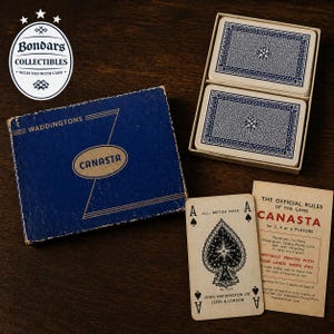 May include: A vintage Canasta card game set. The blue box reads "WADDINGTONS CANASTA". Two decks of cards are in a box with blue patterned backs. Two playing cards and the game rules are visible.